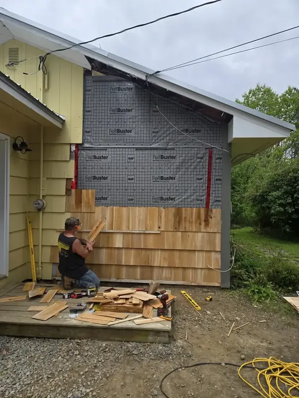 Worker fitting cedar shingle siding to a wall with felt underlayment.
