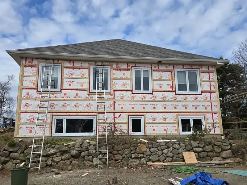 House mid-renovation with house wrap, new windows, and stone foundation.